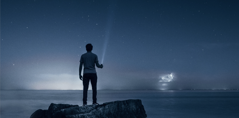 man with flashlight looking at night sky and ocean