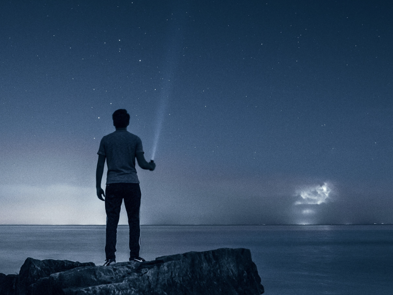 man with flashlight looking at night sky and ocean