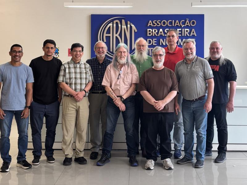 The committee and their guests, Euler and Matheus, pose for a group photo in front of the ABNT logo